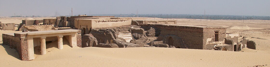 Panoramic view of excavated architectural remains emerging from the desert landscape, highlighting the extent and complexity of the archaeological site.