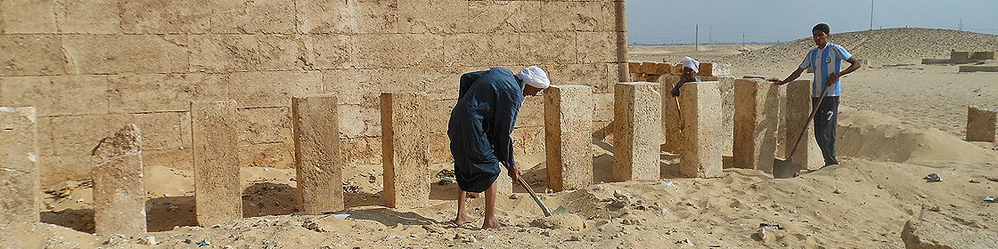 عمال محليون يزيلون تراكمات الرمال حول المنشآت الأثرية أثناء أعمال الحفائر.