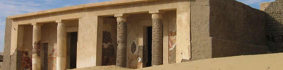 Ancient temple façade with columns and preserved wall paintings partially exposed by the sands.