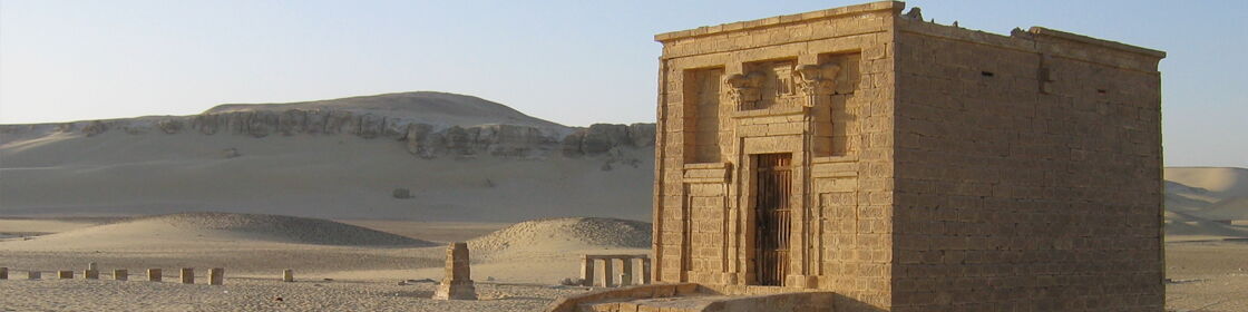 A small stone-built funerary monument standing among the desert landscape of the Tuna el-Gebel necropolis.